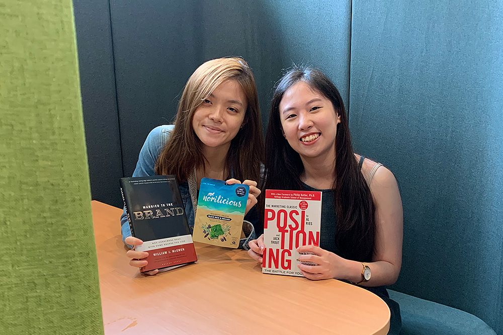BBA Year 4 students Hew Qian Yu (left) and Lee Jia Xin hope to share the value of marketing through the work of NUS MINT. Qian Yu is holding a packet of seaweed snack that they promoted on social media last semester.